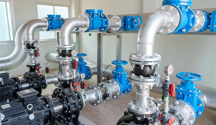 Large industrial water pumps and silver piping with blue valves in a professional facility