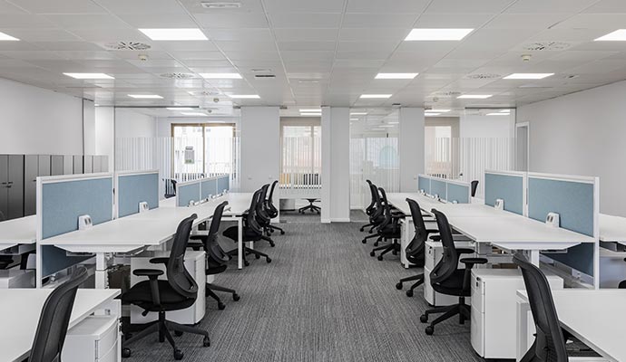A clean, professionally maintained corporate office with rows of white desks and ergonomic chairs