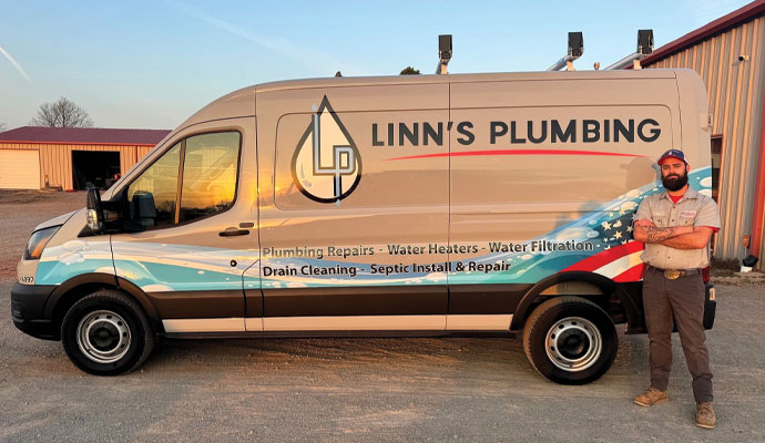 Linn's Plumbing service vehicle parked outside with a team member standing beside it