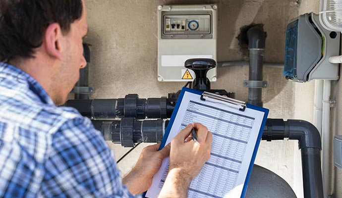 Person inspecting water pipes and writing on an inspection checklist