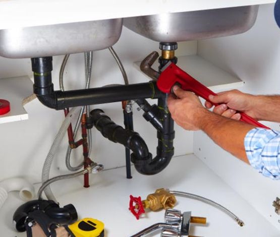 Plumber performing sink repair service Professional plumber repairing a sink using tools in a residential kitchen