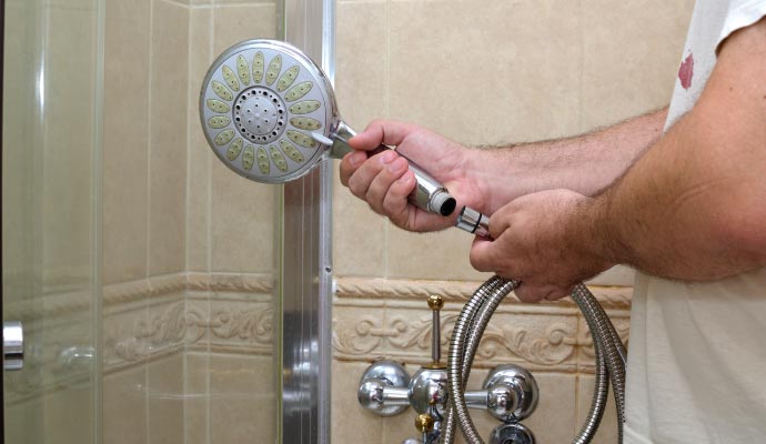 Man installing new handheld shower head in bathroom Man installing new handheld shower head in bathroom
