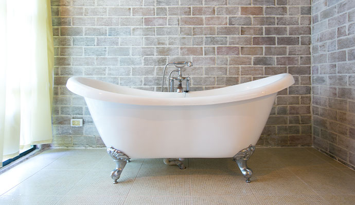 White clawfoot freestanding bathtub against brick wall