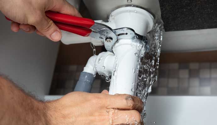 Person repairing plumbing under sink with equipment